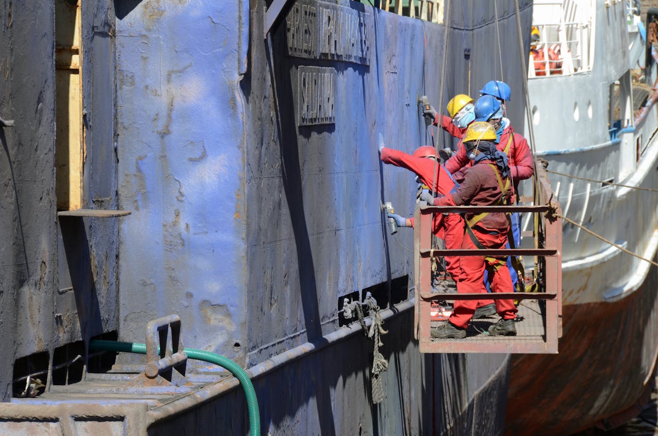 men on a hanging platform repairing the outside of a ship in a shipyard 6638576.jpeg